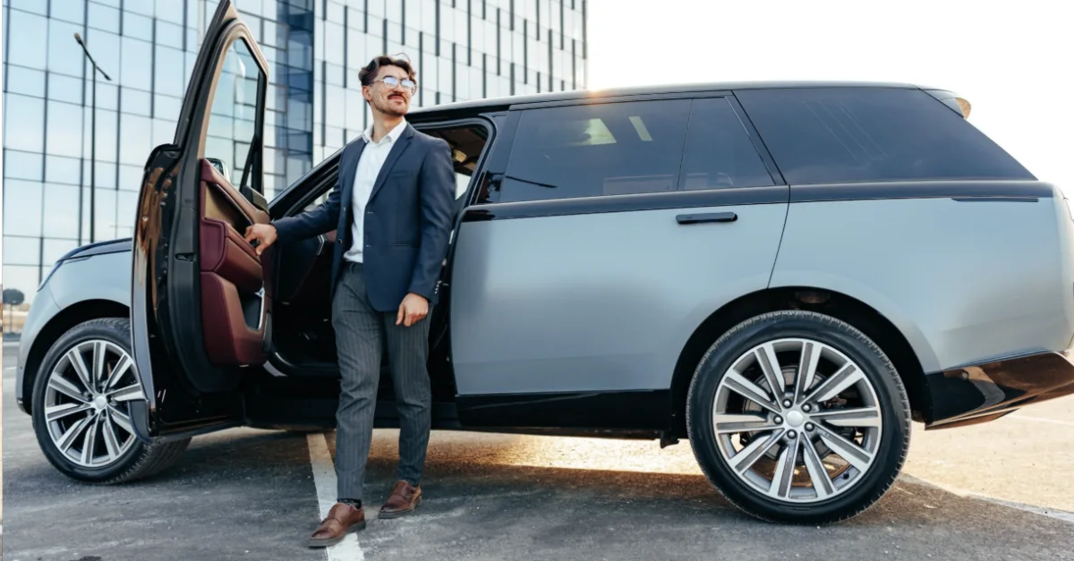 An individual standing beside an open car door while stepping out of a luxury SUV in an urban business district.