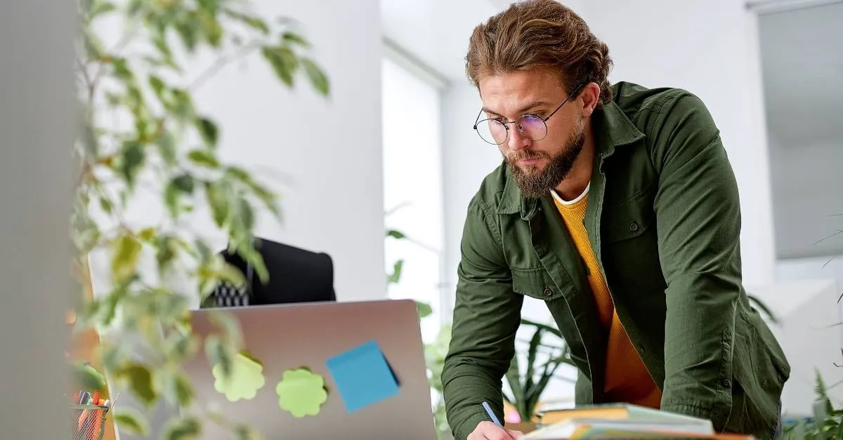 HR manager standing, leaning over working on laptop in office