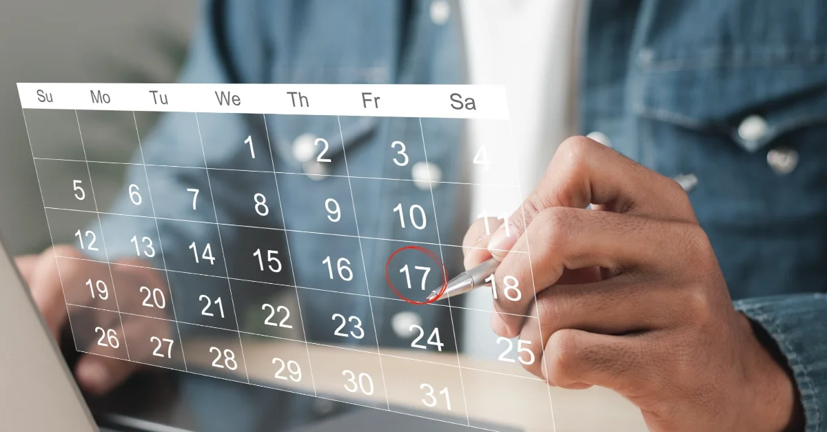 Individual using a stylus to mark a date on a digital calendar while working on a laptop.