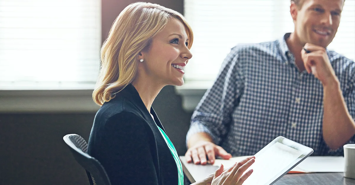 Two colleagues sitting together in an office, reviewing information on a digital tablet during a meeting.