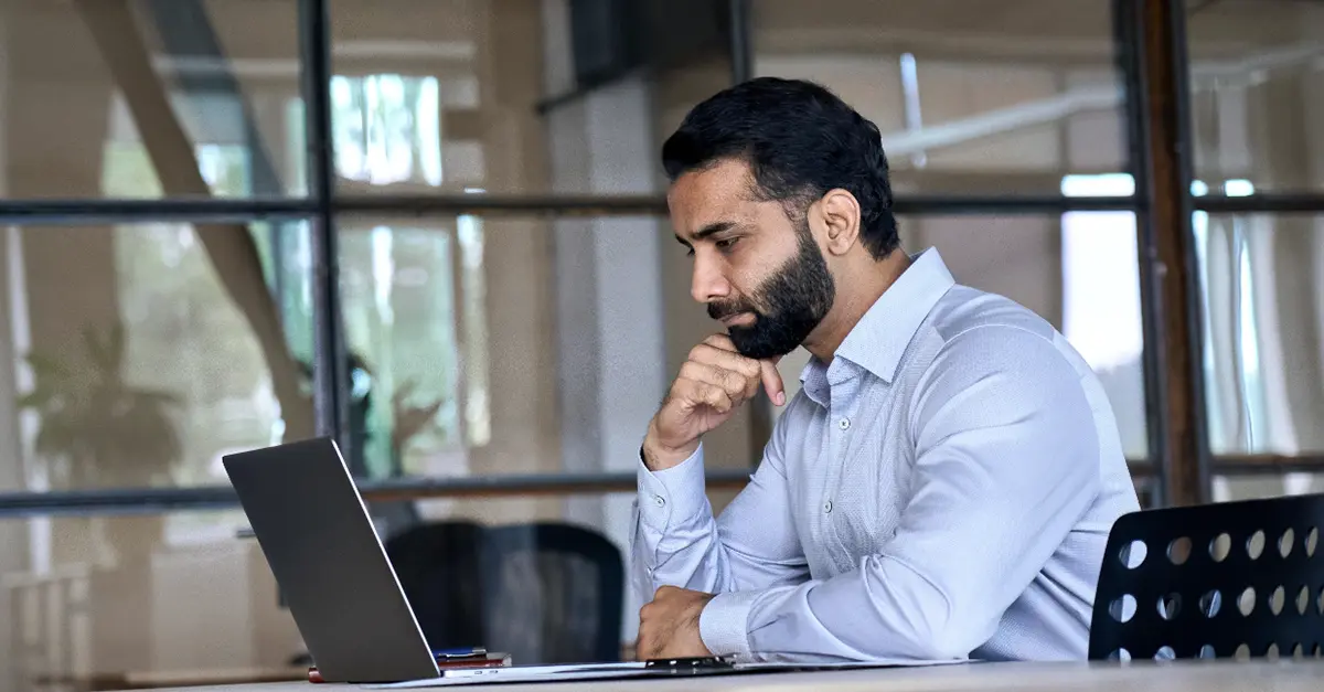 Person seated at a desk using a laptop in a modern office with glass partitions and natural light.