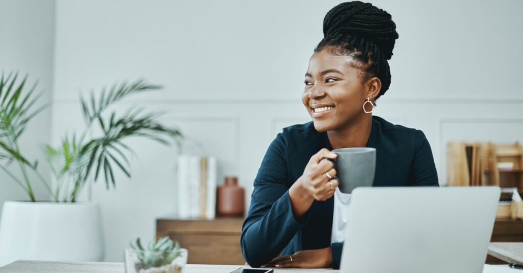 HR professional smiling while holding cup of coffee in front of laptop