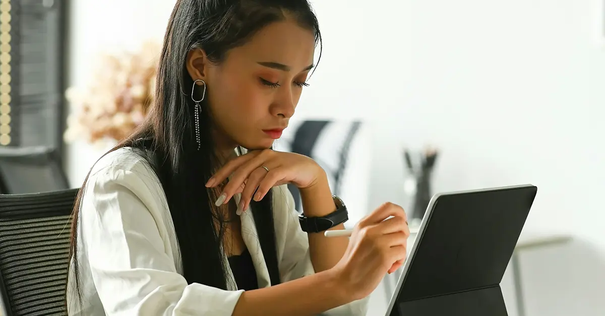 Individual seated at a desk using a digital tablet with a stylus in a bright office setting.