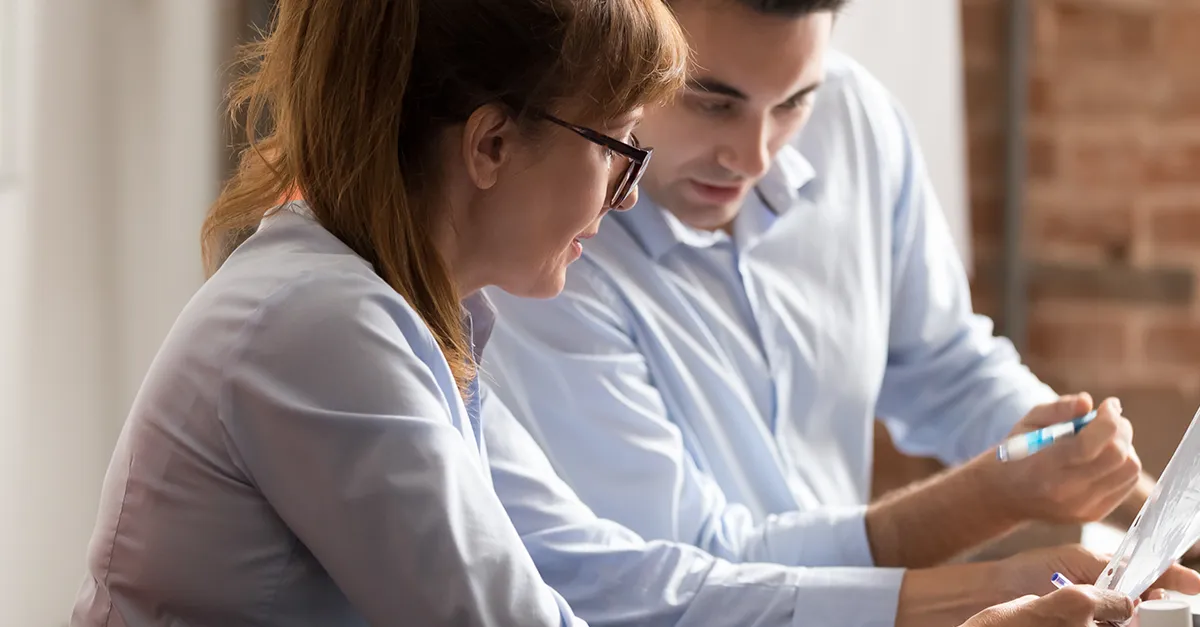 Two colleagues collaborating and reviewing documents together at a desk.