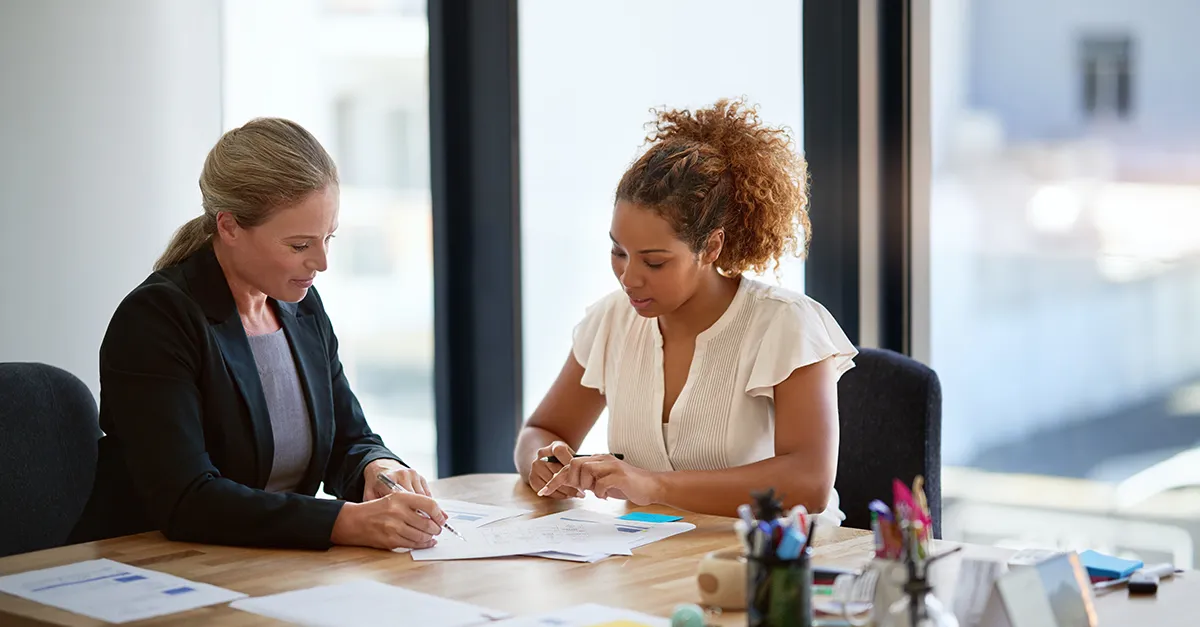 Two professionals discussing documents together at a desk in a bright office.