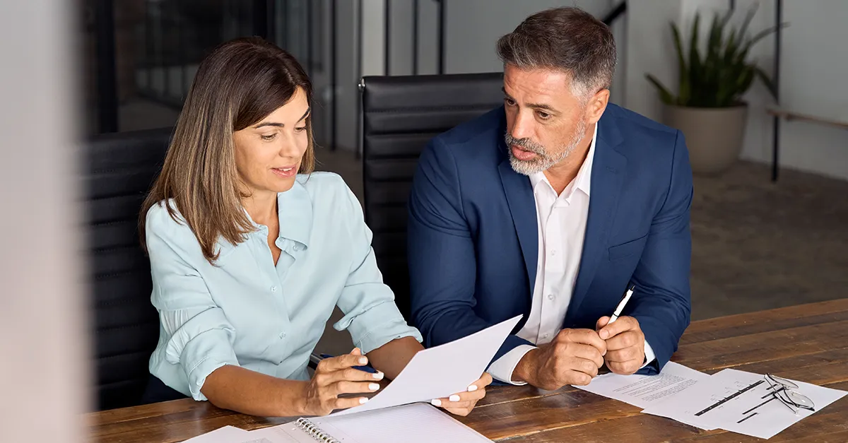 Two professionals reviewing documents together at a desk during a meeting.