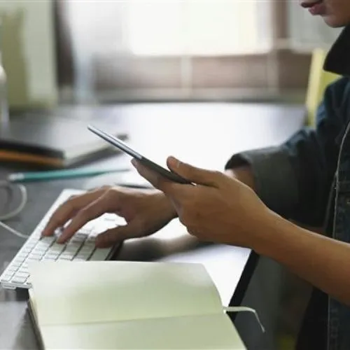 HR professional in the manufacturing industry working on a computer and looking at a mobile phone