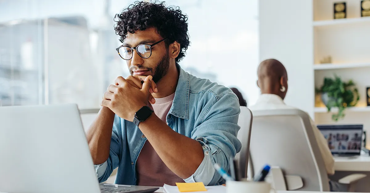 Person sitting at a desk and working on a laptop in a modern office environment.