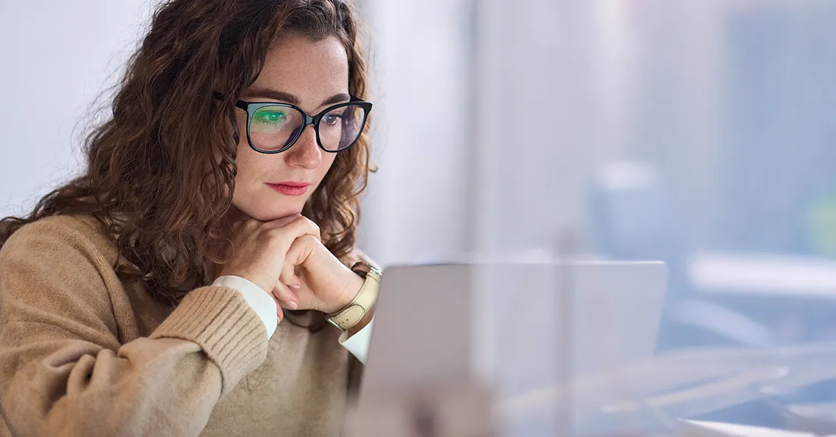 Person sitting at a desk and working on a laptop in a bright office environment.
