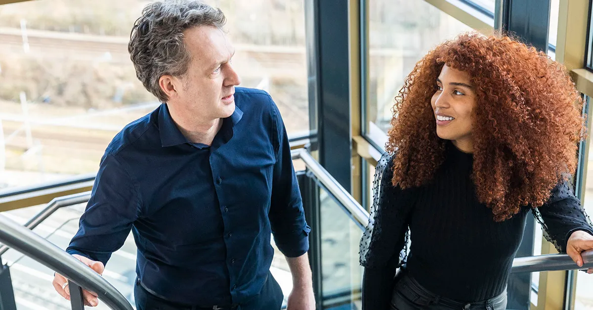 Two coworkers walking up a staircase inside a modern office building.