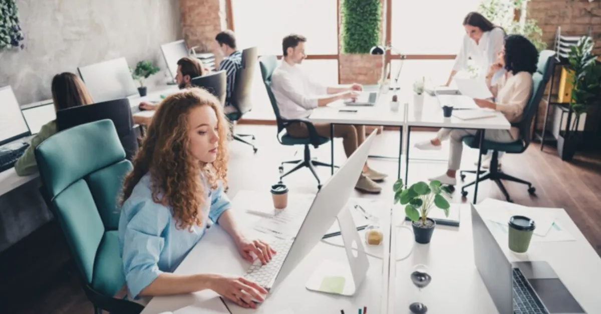 Employees working at desks in a bright open‑plan office, using computers and collaborating in a modern workspace.