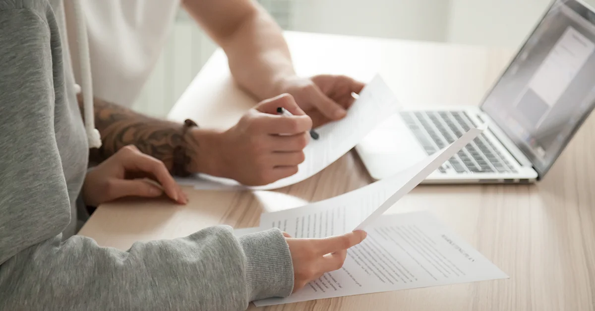 Two people sitting at a desk reviewing documents together with a laptop open in front of them.