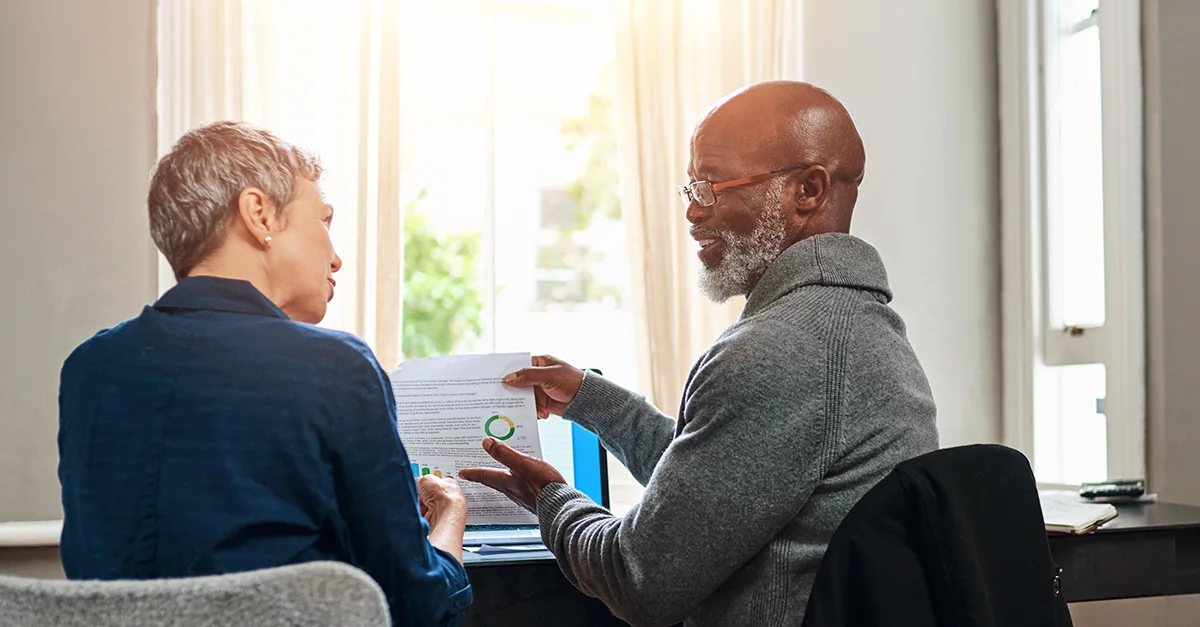 Two colleagues sitting by a window reviewing a printed report together in an office setting.