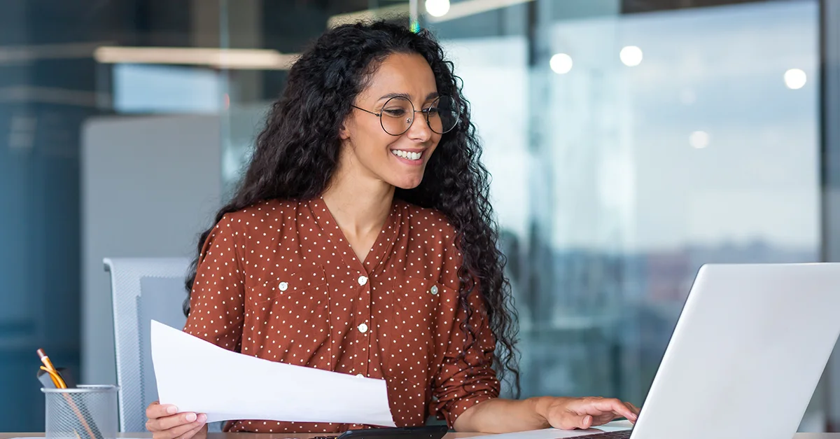 Person reviewing printed documents while working on a laptop in a modern office.