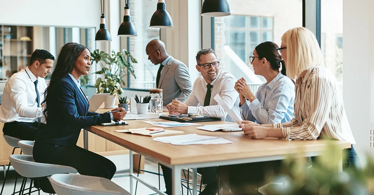 Colleagues engaged in a collaborative discussion around a large table in a bright, modern office space.
