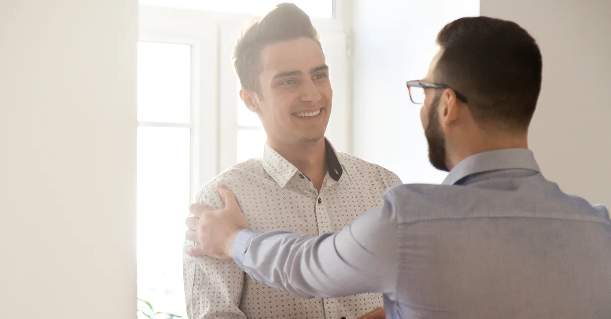 One colleague placing a hand on another’s shoulder while having a serious conversation in a bright office space.