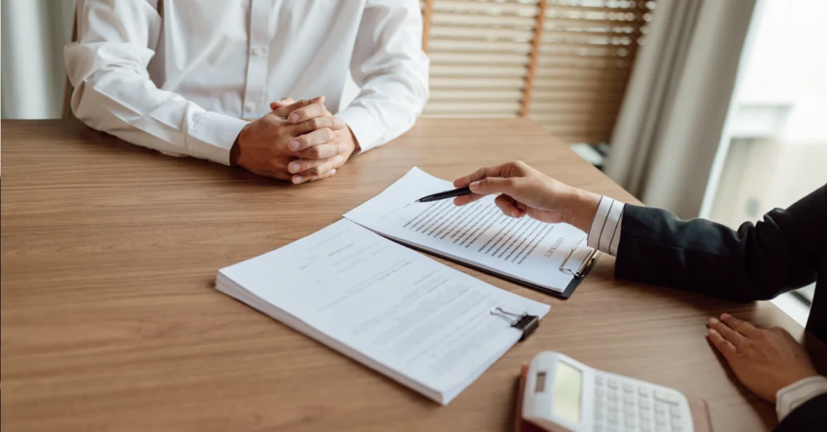 Two people sitting across a desk during a meeting, reviewing documents while one person points to a section on a form beside a calculator.