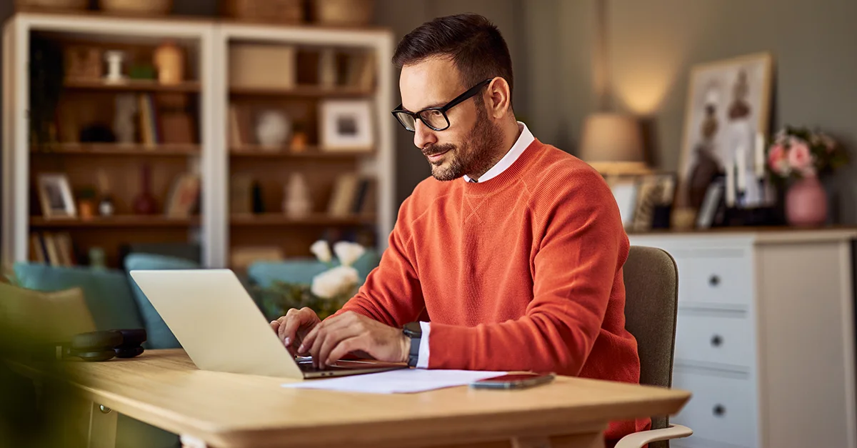 Person working on a laptop at a wooden desk in a home office