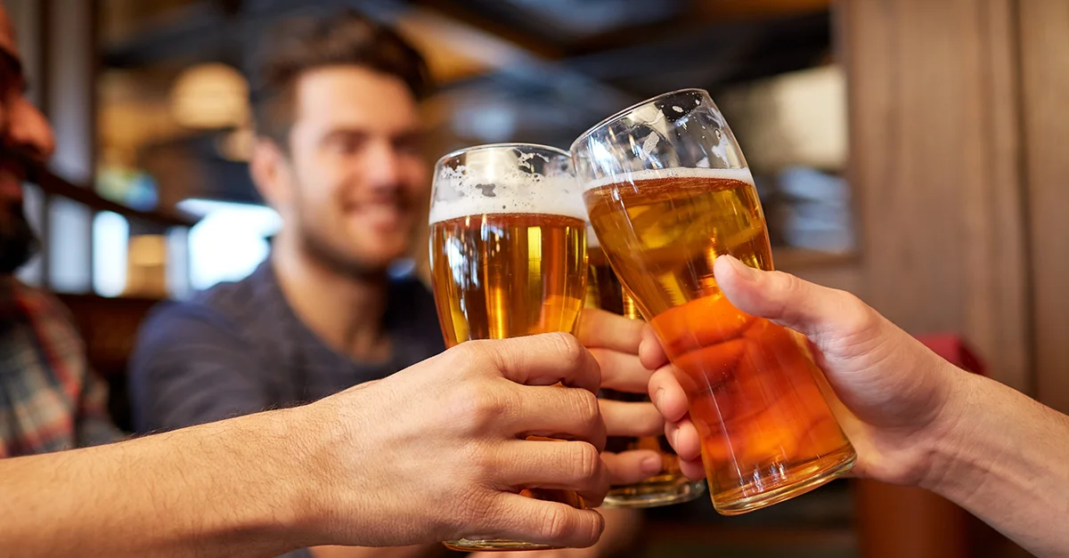Several hands holding beer glasses raised together in a social setting.
