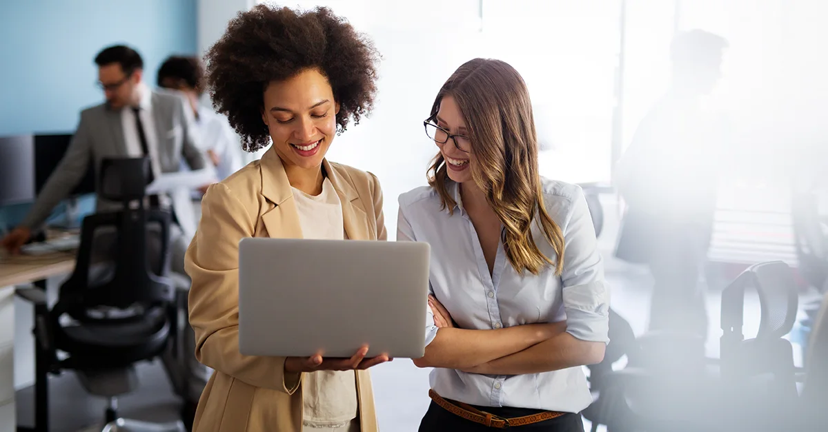 Two professionals standing together in an office, reviewing information on a laptop