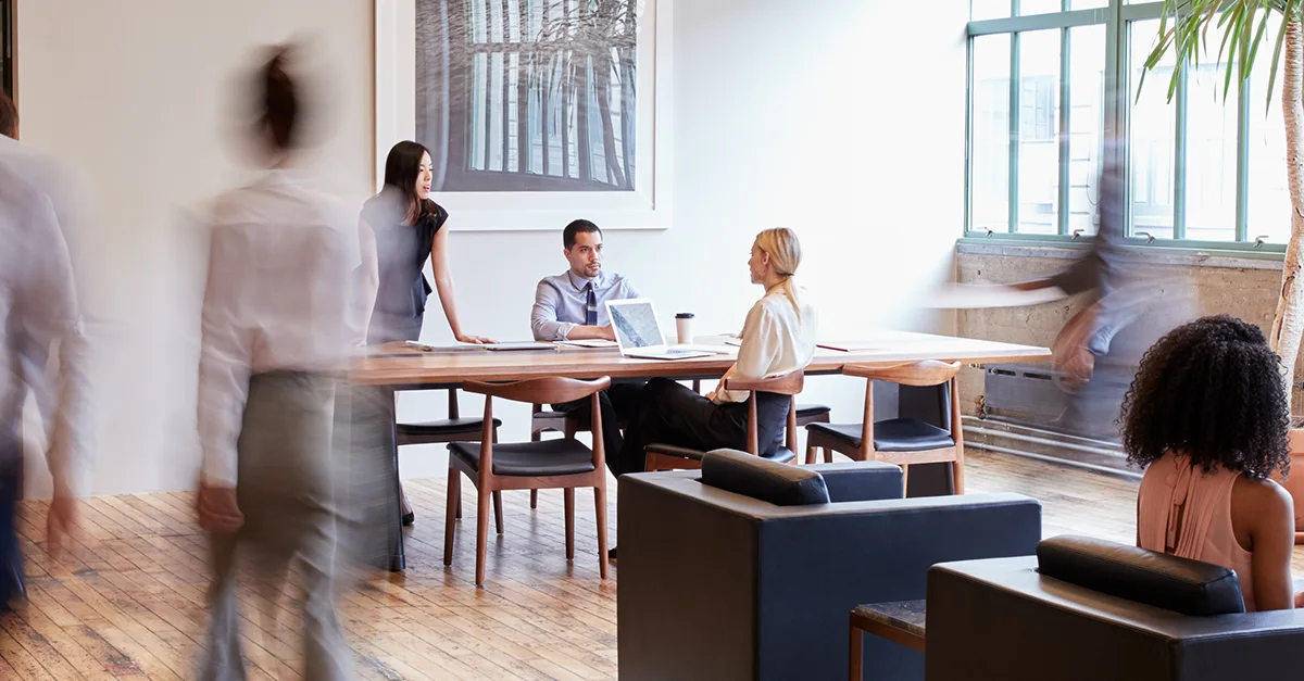 Team meeting in a modern office with people moving in background