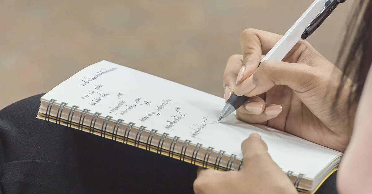 Person writing notes in a notebook with a pen