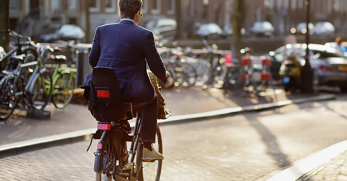 An individual riding a bicycle along a city street, with parked bicycles and buildings visible in the background.