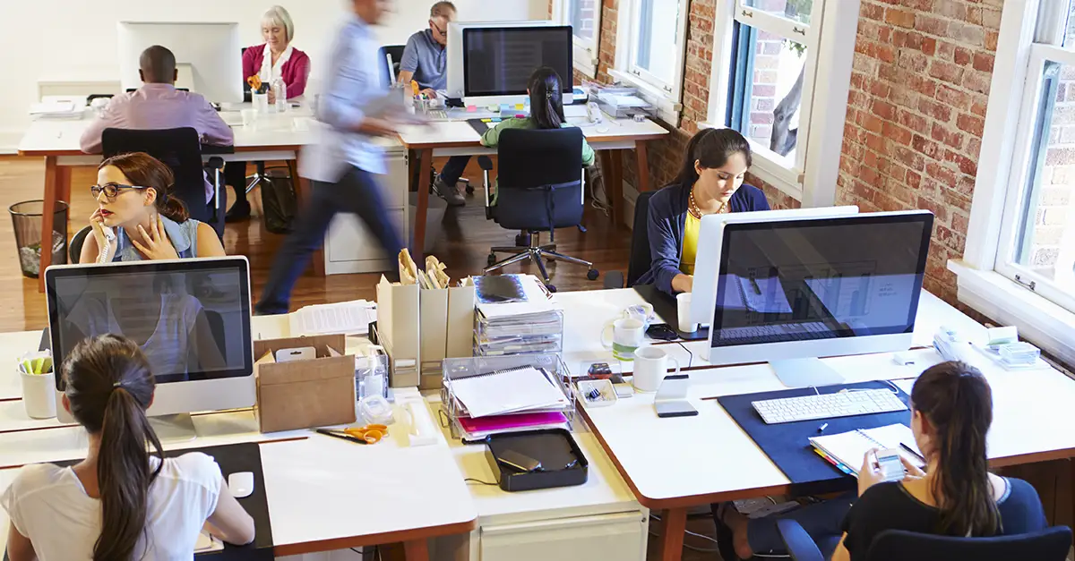 People working at desks with desktop computers in an open-plan office workspace