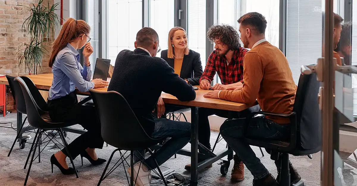 Group of people seated around a table in a modern office, discussing documents during a meeting.