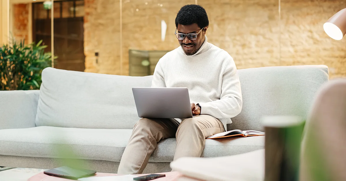 Person seated on a sofa using a laptop in a modern indoor workspace with soft lighting.