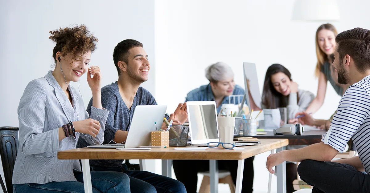 Group of coworkers gathered around a table using laptops and documents during a collaborative office meeting.