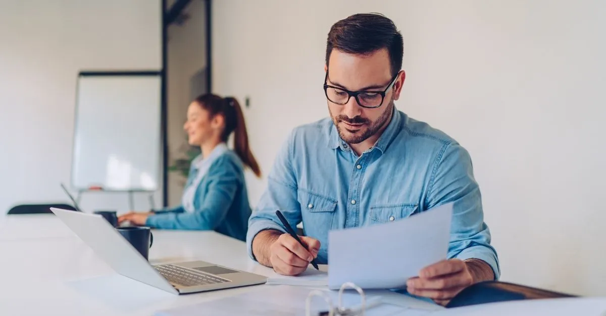 Male HR professional reviewing paperwork in office with female colleague behind