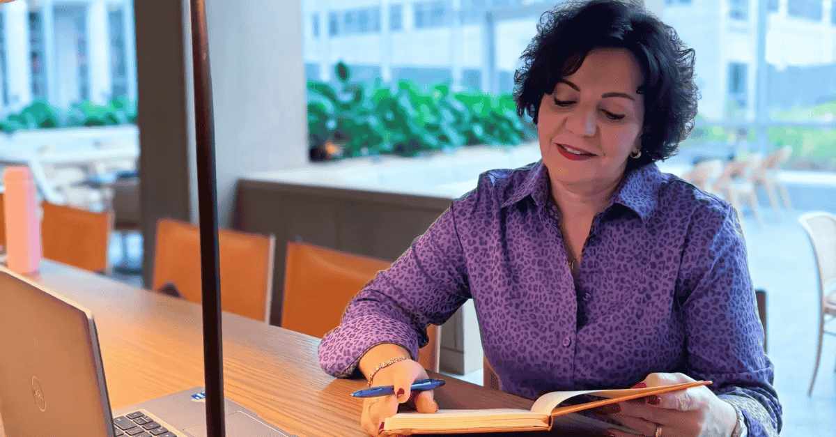 Brightmine employee in purple shirt writes notes in journal at desk.